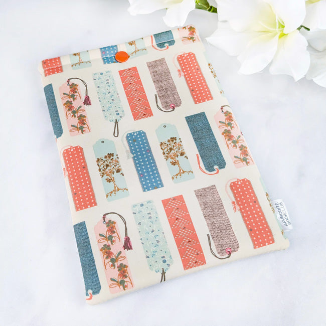 Kindle Paperwhite sleeve featuring a whimsical pattern of vintage-style bookmarks in coral, teal, and soft brown tones on a cream background.