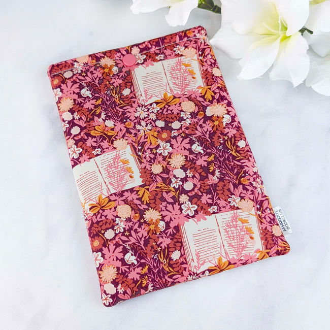 Fabric Kindle sleeve with a burgundy and pink floral pattern featuring open books, displayed on a white surface with white flowers.