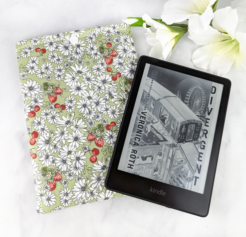 padded kindle paperwhite sleeve with snap. fabric features white daisy flowers, tiny cherries and strawberries on a sage green background.