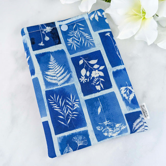 Kindle sleeve with a deep blue and indigo fabric featuring white botanical print blocks, shown with white flowers in the background.