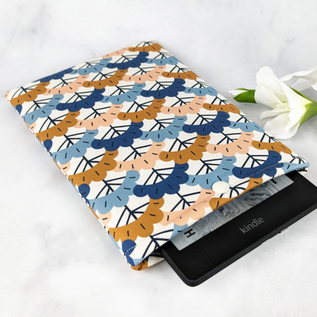 Kindle sleeve with a repeating pattern of stylized ginkgo leaves in shades of navy, mustard, dusty pink, and blue on a cream background.
