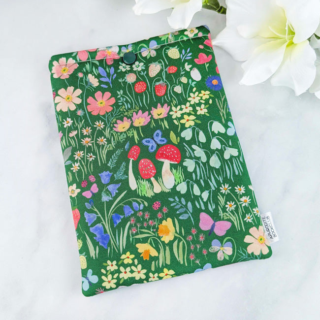 Kindle Paperwhite sleeve with a whimsical meadow design featuring colorful wildflowers, strawberries, and greenery on a rich green background.