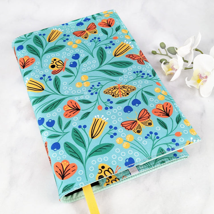 adjustable fabric book cover, fabric pattern shows yellow and orange flowers and butterflies on light turquoise background.