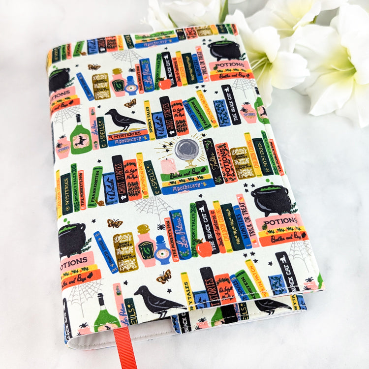 book cover decorated with colorful illustrated books, potion bottles, ravens, and spell labels in a playful witchy library design.