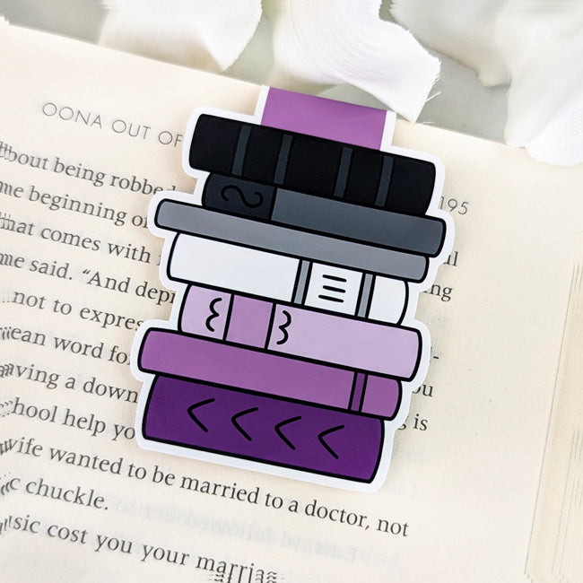 Magnetic bookmark shaped like a vertical stack of books in asexual pride colors—black, gray, white, and purple—clipped to the top of an open book.