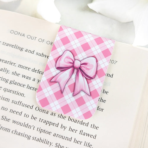 Magnetic bookmark featuring a pink satin bow design set against a pink argyle background, clipped to the top of an open book.