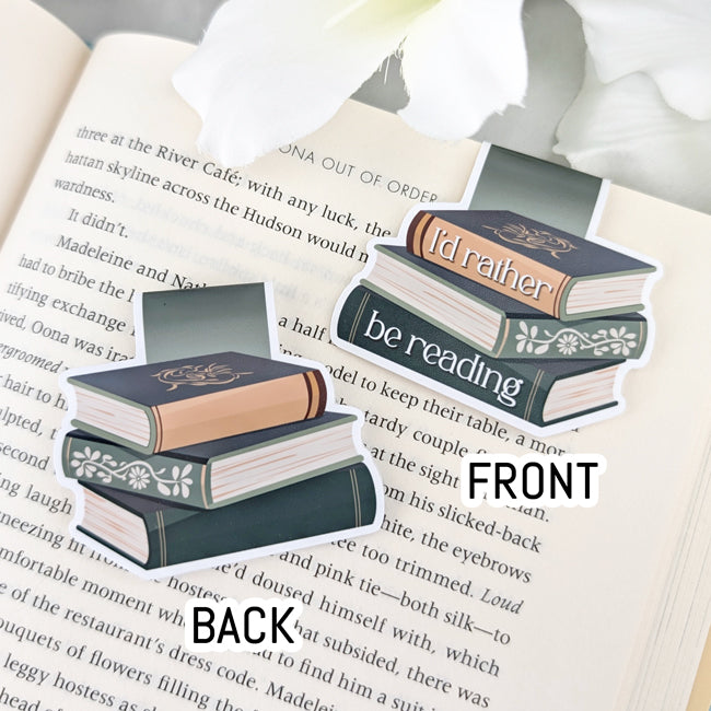 Front and back view of a magnetic bookmark with a sage green and brown book stack design that reads 'I'd rather be reading,' displayed on an open book.