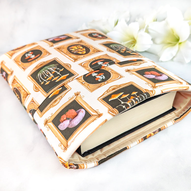 Cream book sleeve featuring framed mushroom illustrations in ornate golden borders, creating a whimsical naturalist gallery design.