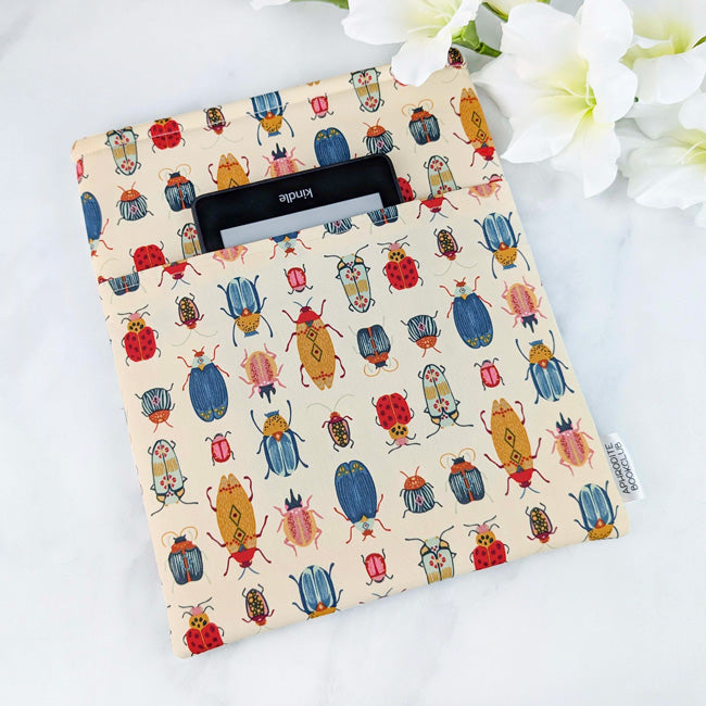 Fabric book sleeve with a playful entomology-inspired print featuring colorful beetles, ladybugs, and other whimsical bugs on a soft cream background.