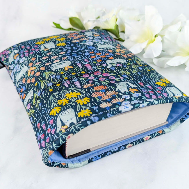 Fabric sleeve with a navy blue background featuring cats and colorful wildflowers, displayed on a white surface with white flowers.