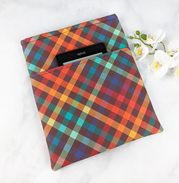 large padded book sleeve with pocket, fabric pattern features bold plaid pattern in shades of red, brown, orange, teal and green.