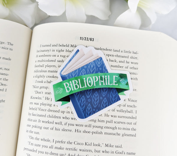 Bibliophile vinyl sticker with a blue book and green ribbon placed on the open pages of a novel.