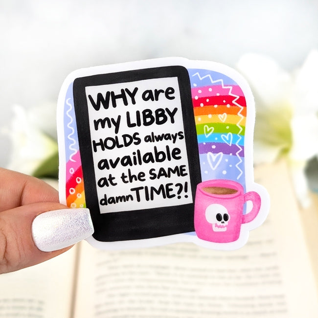Colorful vinyl sticker with rainbow background and e-reader screen text “Why are my Libby holds always available at the same damn time?!” with a pink coffee mug, held in hand over an open book.