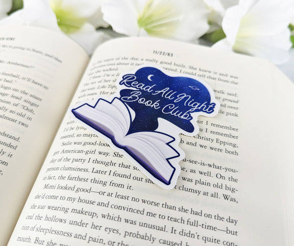 Read All Night Book Club vinyl sticker featuring an open book with starry night sky design, placed on the pages of a novel.