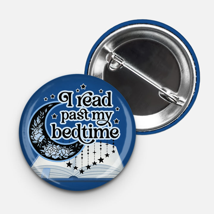 Round pinback button with a dark blue background featuring the phrase “I read past my bedtime” in bold white text. The design includes a decorative crescent moon with floral accents, an open book, and hanging stars, evoking a dreamy nighttime reading vibe. The back of the button with a standard metal pin is also shown.