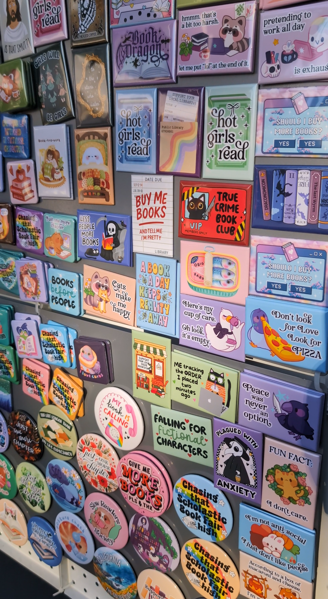 Display board filled with colorful book-themed magnets featuring playful quotes, illustrations, and pastel designs arranged neatly on a gray metal surface.