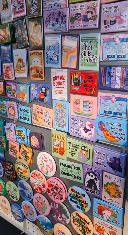 Display board filled with colorful book-themed magnets featuring playful quotes, illustrations, and pastel designs arranged neatly on a gray metal surface.