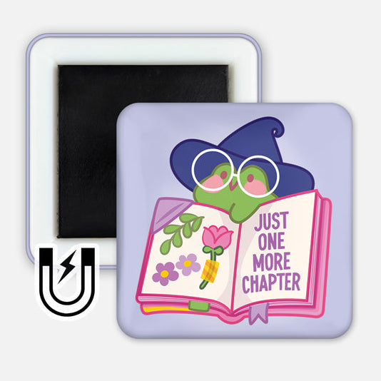 A square magnet featuring a cute frog wearing a witch hat and round glasses, peeking over an open book. The book has colorful flowers on one page and the text "JUST ONE MORE CHAPTER" on the other. The background is a soft lavender color, and a small magnet icon is displayed in the corner, indicating the product type.