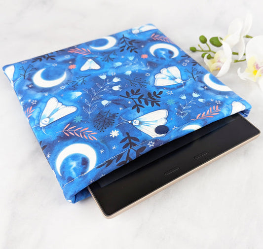 padded kindle oasis sleeve with snap. fabric showcases whimsical illustrations of moths, florals and moons on a blue background.