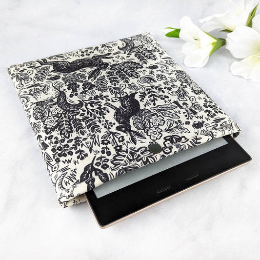 padded kindle oasis sleeve with snap. fabric showcases monochromatic vintage style line art featuring woodland elements like rabbits, squirrels and foliage on a off-white background.