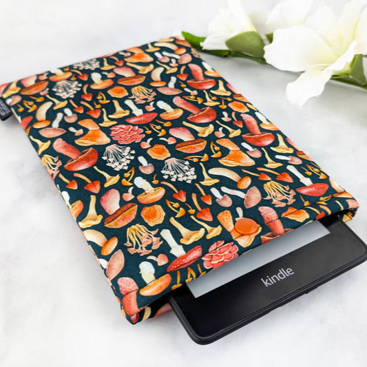 padded Kindle sleeve with snap, fabric features various fall mushrooms in shades of red and orange on a dark navy background.