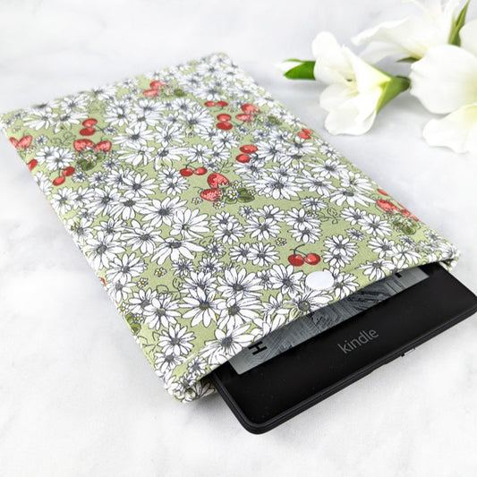 padded kindle paperwhite sleeve with snap. fabric features white daisy flowers, tiny cherries and strawberries on a sage green background.