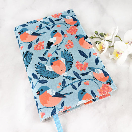 Fabric book cover featuring a charming pattern of bullfinch birds perched on berry branches, in shades of coral, navy, and blue on a soft blue background, finished with a light blue ribbon bookmark.