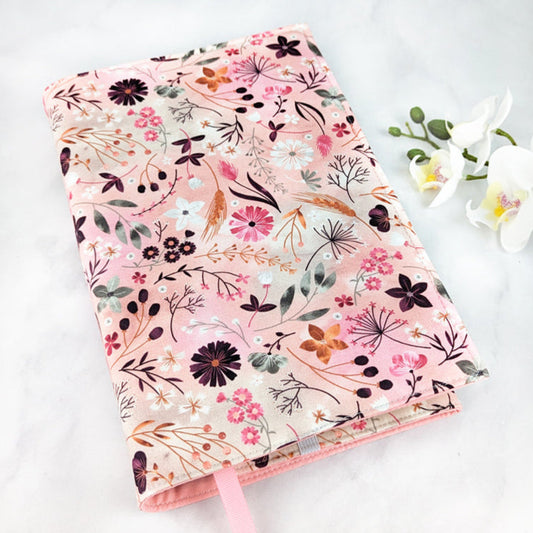 large adjustable fabric book cover, fabric features various fields flowers on a light pink watercolor background.