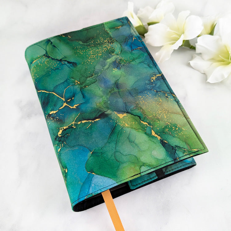 large adjustable fabric book cover, fabric showcases green and teal marble texture with gold accents.