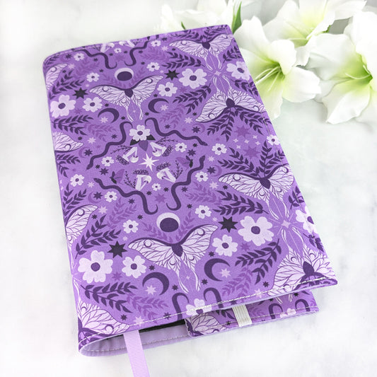 Lavender purple book cover with a celestial moth and floral pattern featuring moons, stars, vines, and blossoms in deep violet tones.