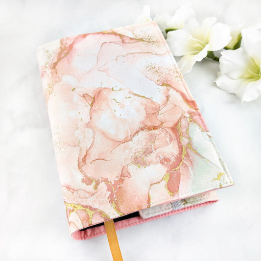 Fabric book cover with a soft, dreamy watercolor design in blush pinks and subtle greens, accented by gold marbling details, and finished with a golden yellow ribbon bookmark.