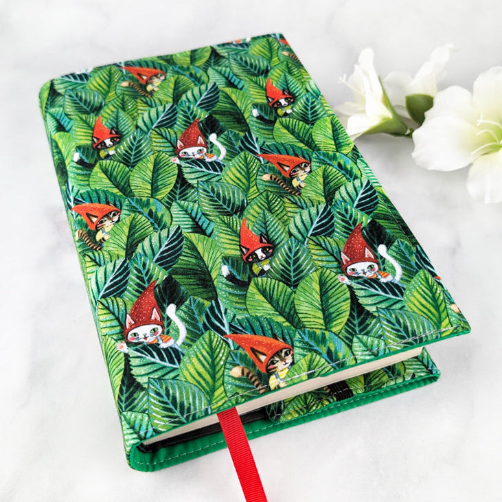 large adjustable fabric book cover, fabric features cute cats in red gnome hats hidden among bold green leaves.