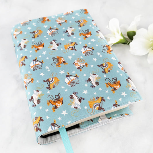 large adjustable fabric book cover, fabric showcases orange and white roller blades and tiny white stars on a dusty blue background.