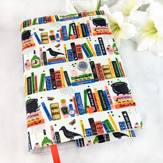 book cover decorated with colorful illustrated books, potion bottles, ravens, and spell labels in a playful witchy library design.