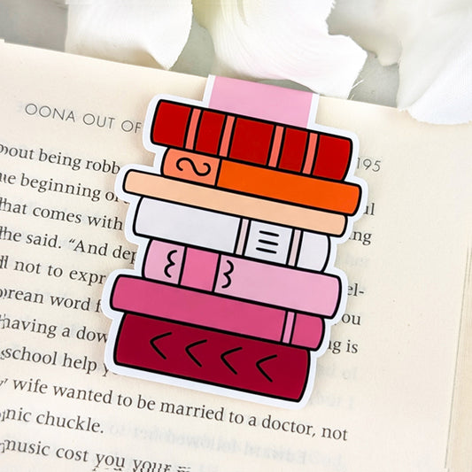 Magnetic bookmark shaped like a vertical stack of books, each book featuring a different shade from the lesbian pride flag, clipped over an open book page.
