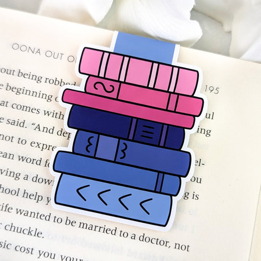 Magnetic bookmark shaped like a vertical stack of books, clipped to the top of an open book. The spines are colored in shades of pink, purple, and blue, representing the omnisexual Pride flag.