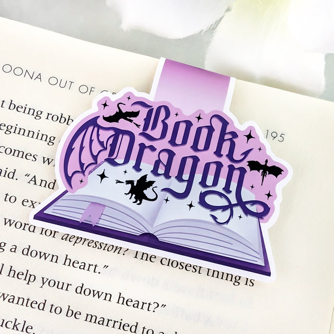 Purple magnetic bookmark with the phrase “Book Dragon” in gothic lettering, featuring flying dragons, stars, and an open book illustration.