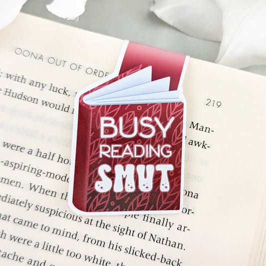 magnetic bookmark shaped like a red book with 'Busy Reading Smut' text, clipped to an open book.