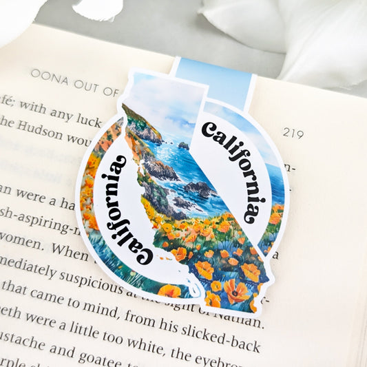 Magnetic bookmark shaped like California with coastal scenery and poppy flowers, featuring the word 'California' in bold script on a round background.