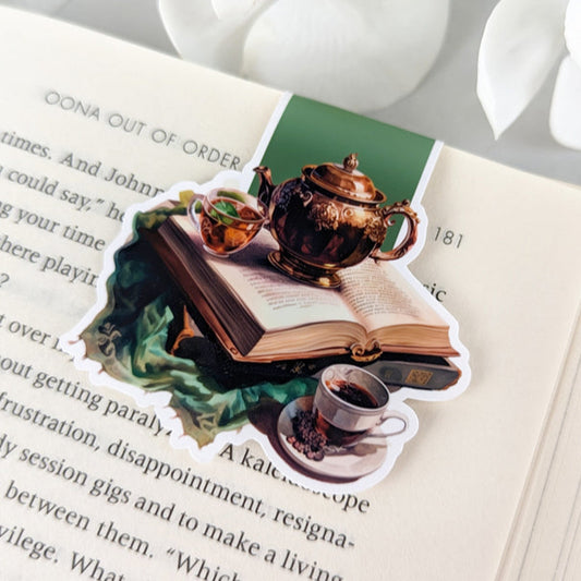 magnetic bookmark featuring a teapot, teacup, and a book, laying on pages of an open book.