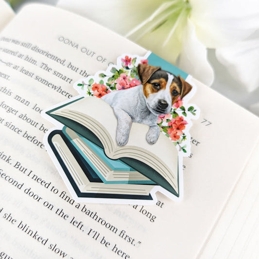 A magnetic bookmark featuring a Jack Russell Terrier puppy peeking out from behind a stack of books. The bookmark has a whimsical, hand-drawn style with floral accents.