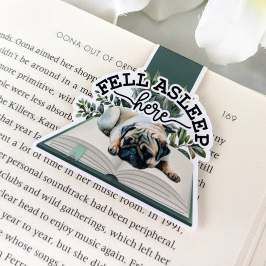 A close-up of a colorful magnetic bookmark featuring a pug dog sleeping on a book. The bookmark has the text "Fell Asleep Here" written on it.