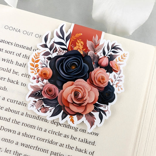 A floral magnetic bookmark featuring black and blush roses with autumn accents, resting on an open book.