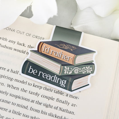 Magnetic bookmark featuring a vintage-style book stack with the phrase 'I'd rather be reading,' clipped to an open book.