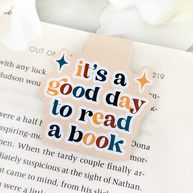 magnetic bookmark featuring a phrase "It's a good day to read a book" written in colorful retro letters on a cream background.