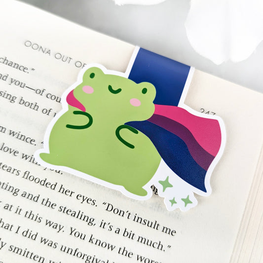 A magnetic bookmark featuring a cute green frog with a smiling face and a flowing Bisexual Pride Flag cape.