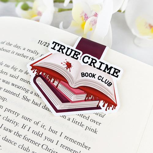 Magnetic bookmark shaped like a stack of books with an open blood-splattered book on top and the phrase 'True Crime Book Club,' clipped to an open book.