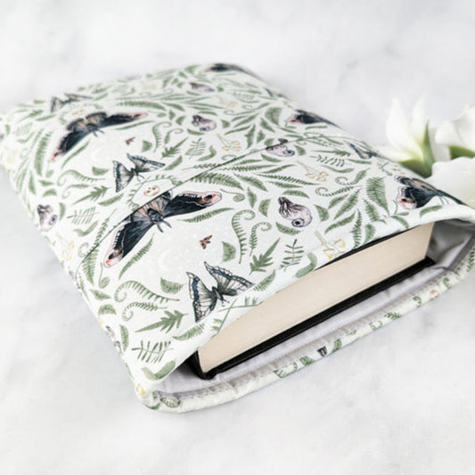 large padded book sleeve with pocket,  fabric pattern featuring ferns, moths, mushrooms, owls and skulls on a light green background.