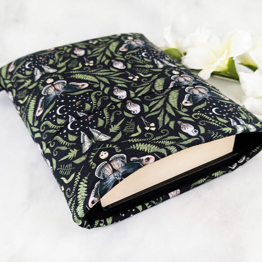 large padded book sleeve with pocket,  fabric pattern featuring ferns, moths, mushrooms, owls and skulls on a black background.