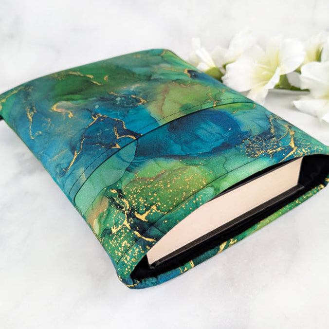 large padded book sleeve with pocket. fabric showcases green and teal marble texture with gold accents.